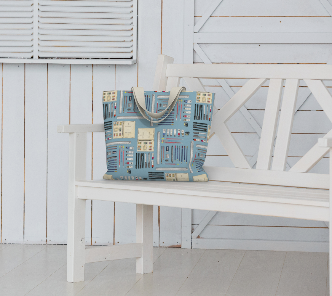 Art Supplies in a repeating pattern on a light blue background. Large market tote bag sitting on a white garden bench..